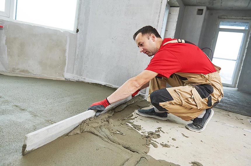 Plasterer smoothing floor surface with a screeder during concrete floor preparation